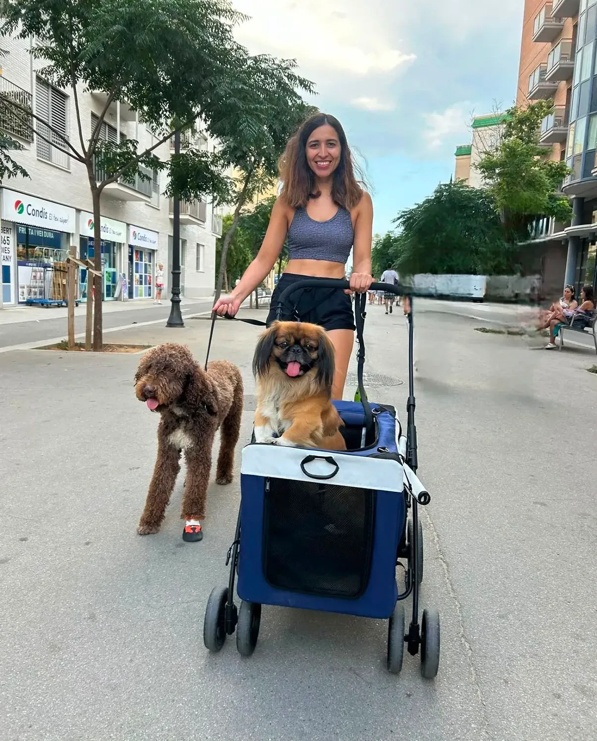 Mariana marchant dans une rue de Barcelone avec un chien d’eau et un pékinois dans sa poussette adaptée